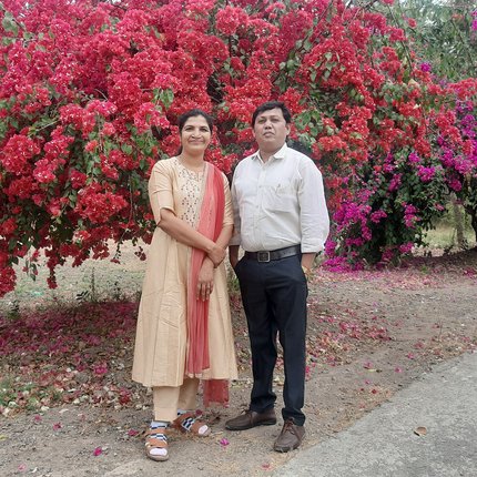 Suresh and Mangala pose together in front of a tree covered in red flowers