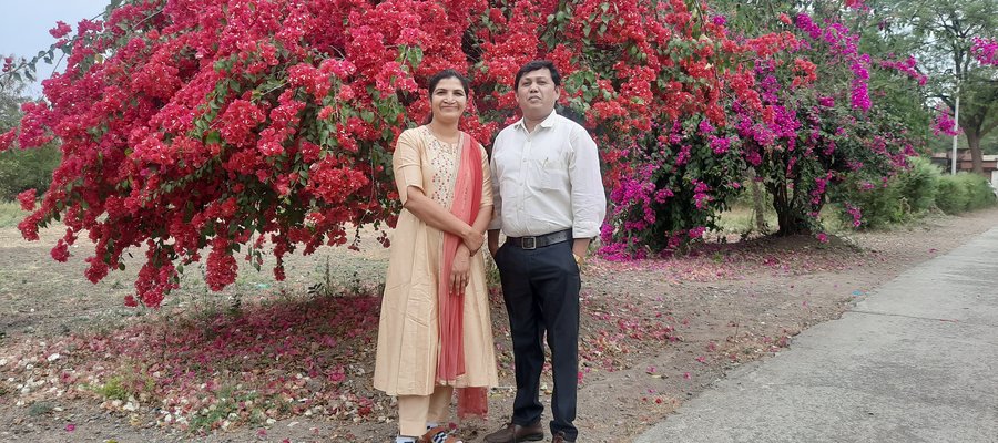 Suresh and Mangala pose together in front of a tree covered in red flowers
