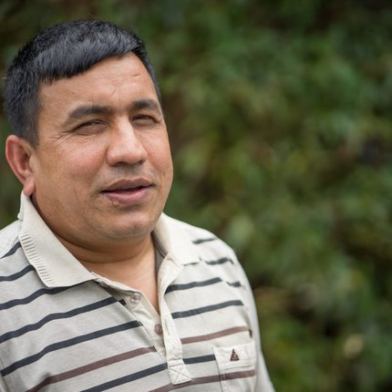 A Nepali man with short black hair wears a striped polo shirt and looks at the camera to his right