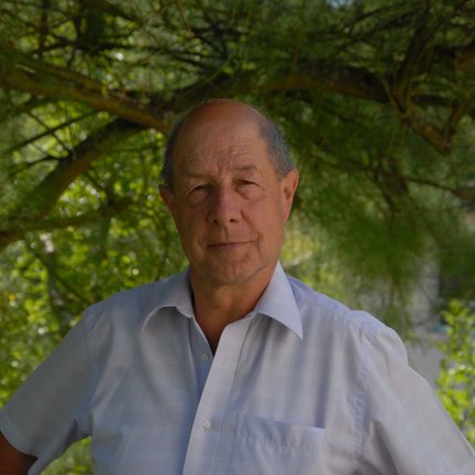 A man in a white shirt standing under a tree looks at the camera