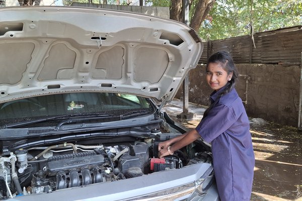 A young girl in a blue suit stands next to a car as she maneuvers one of its engines.