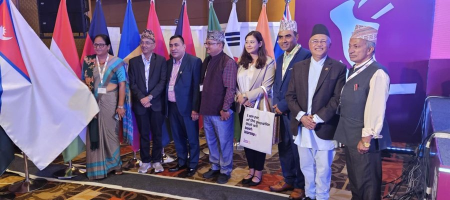 Eight people from Nepal pose for a photo at an event, standing next to a row of flags