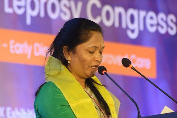 A women from India in bright yellow/green clothes speaks into a podium microphone
