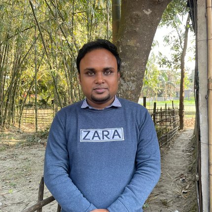 A young Bangladeshi man with a goatee and a blue Zara sweater looks at the camera