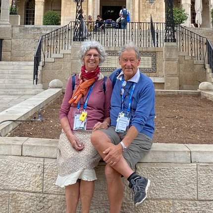 A grey-haired Danish couple sit for a photo in front of the ornate stairs of a YMCA building