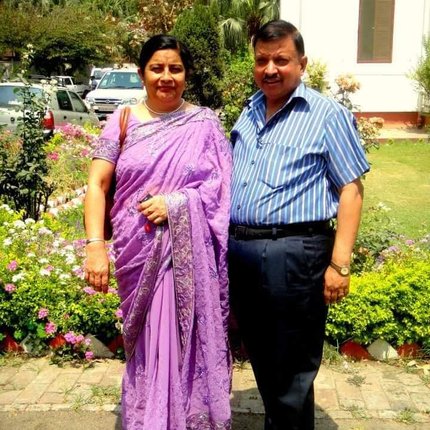 A couple from India pose for the camera on the pavement by a front garden