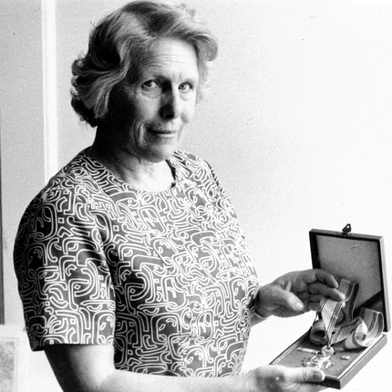 A black and white photo of a woman holding a medal in a presentation box