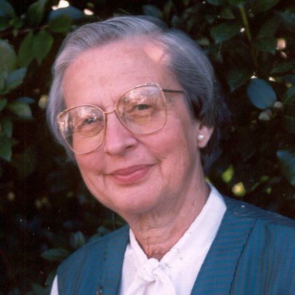 A woman with glasses and grey hair smiles at the camera