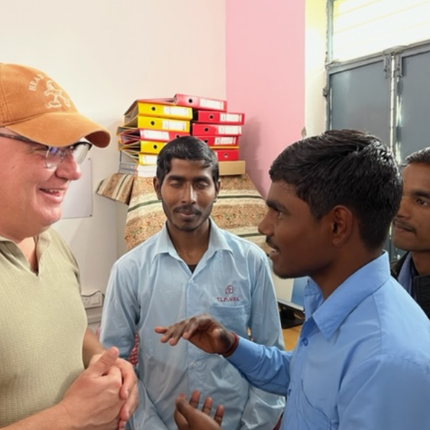 A Danish man in an orange baseball cap, glasses, and a green t-shirt speaks with three men from India who are wearing blue shirts