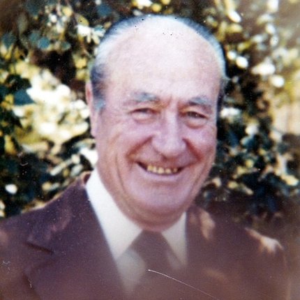 A balding man in a suit and coat smiles at the camera