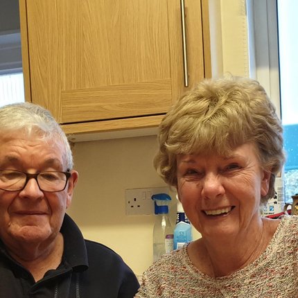 An older white couple smiling at their kitchen table in the UK.