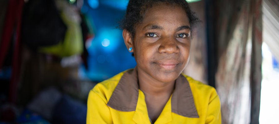 Thresia wears a yellow shirt and looks to camera