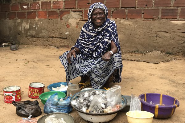 Hawa sits outside her home with the goods she is selling