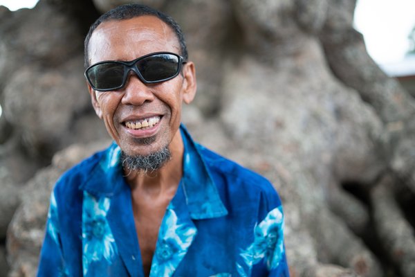 A man from Papua New Guinea wearing a blue shirt and sunglasses smiles at the camera