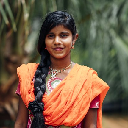 A young woman in an orange sari looks at the camera
