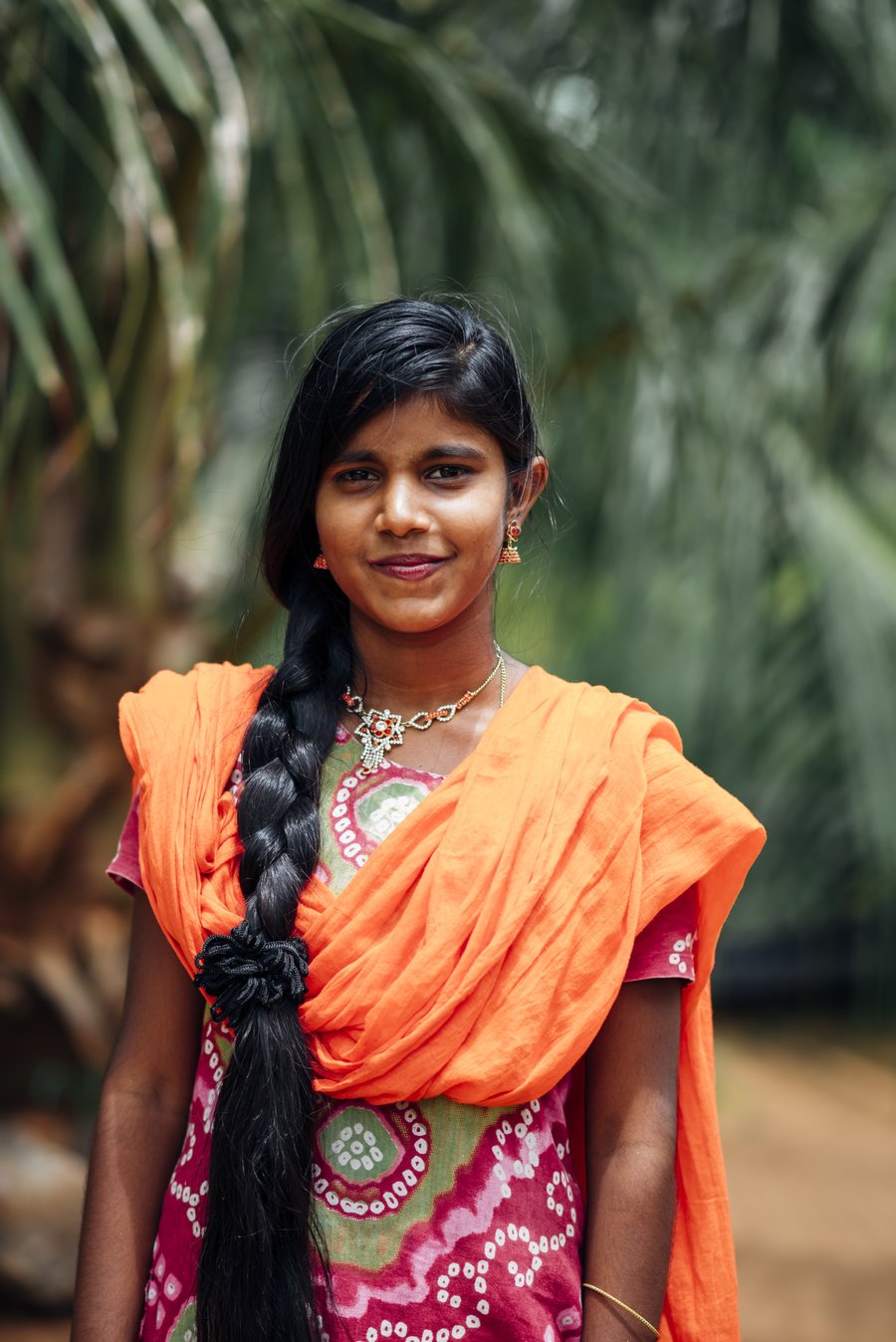 A young woman in an orange sari looks at the camera