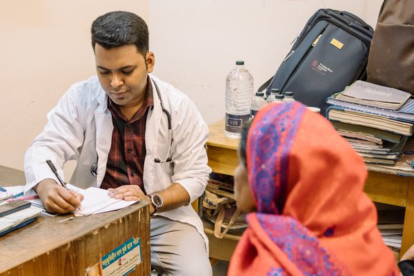 A doctor takes notes during a consultation with a patient in Bangladesh