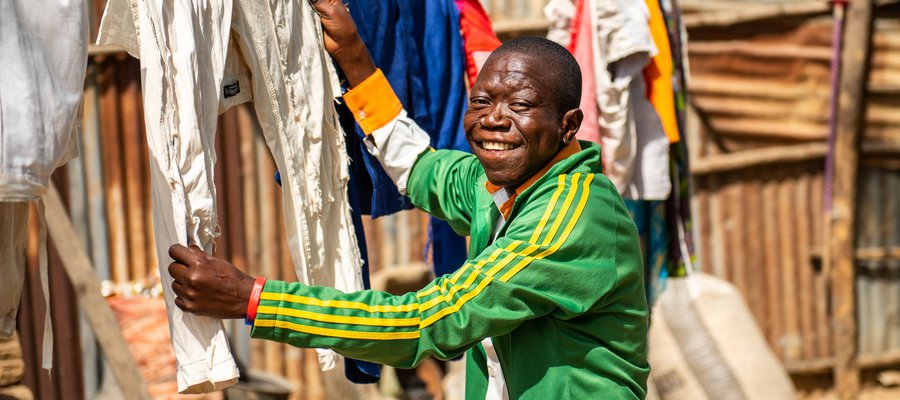 A man smiles at the camera while hanging up clothes to dry