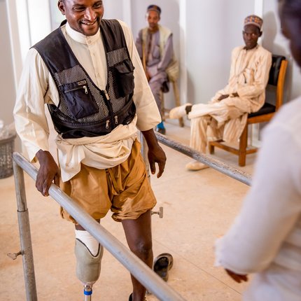 Nuhu holds onto handrails at TLM's workshop as he practices using his new prosthetic leg