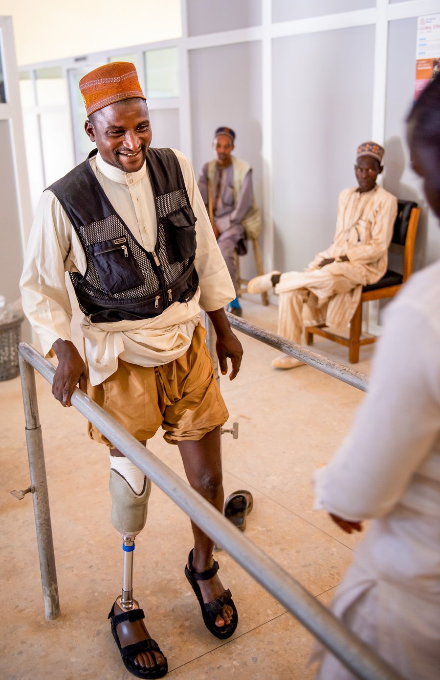 Nuhu holds onto handrails at TLM's workshop as he practices using his new prosthetic leg