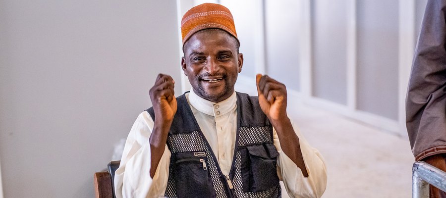 Nuhu sits in a chair, smiling and holding his fists up in celebration at completing a walk with his new prosthetic leg