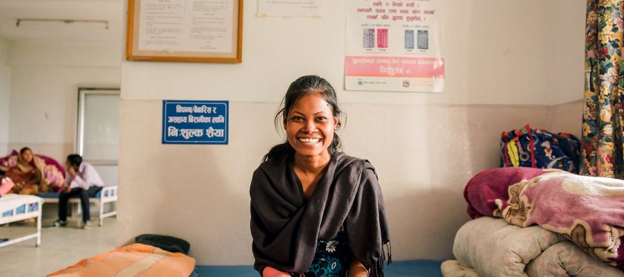 woman sat on a hospital bed, smiling at the camera. He right arm is in plaster of paris