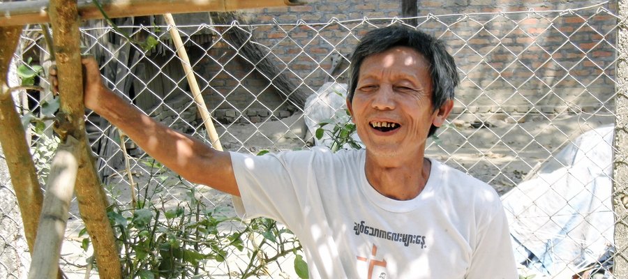 The treasurer of the Myanmar Association of Persons Affected by Leprosy smiles and leans against a tree