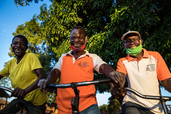Three men in Mozambique stand with their bikes, smiling