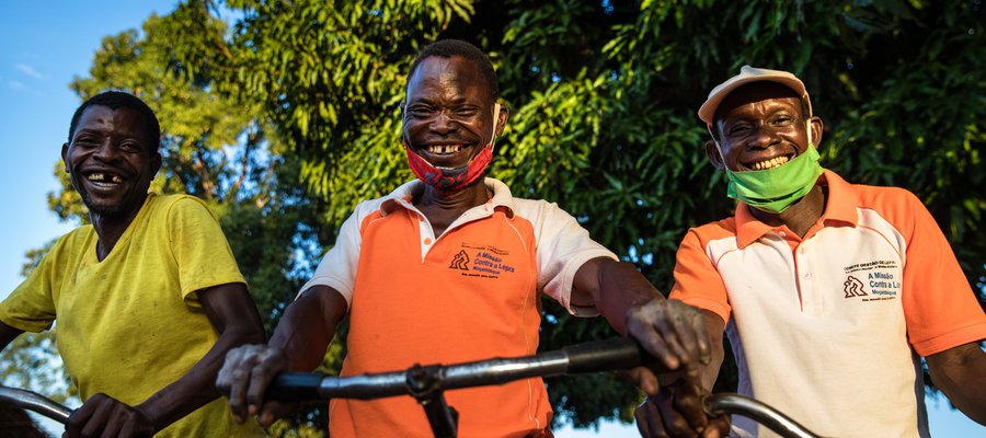 Three men in Mozambique stand with their bikes, smiling