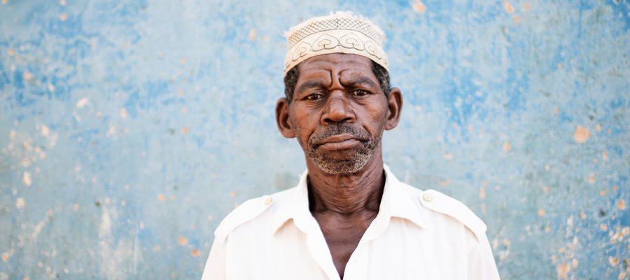 A man in Mozambique stands in front of a faded blue wall