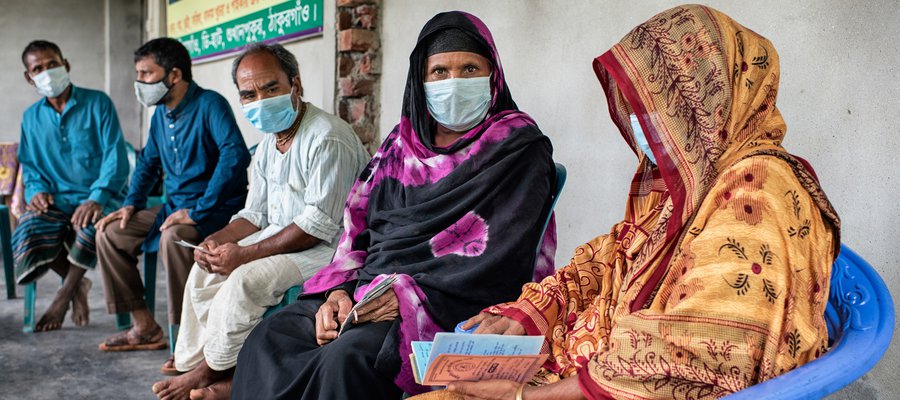 Self-help group members in Bangladesh meet together, sat in a group in plastic chairs