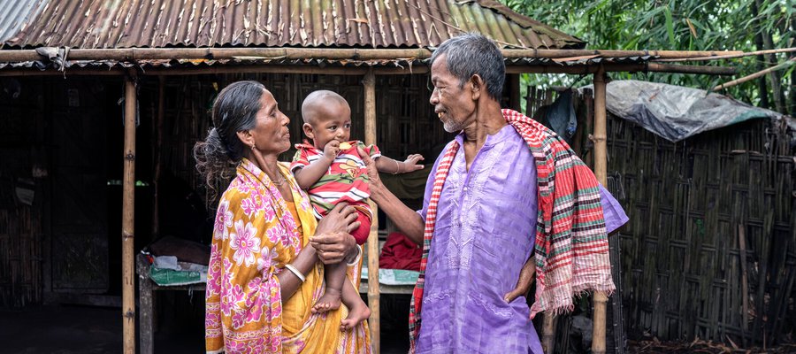 A grandmother in a village in Bangladesh holds her grandson while her husband talks to him