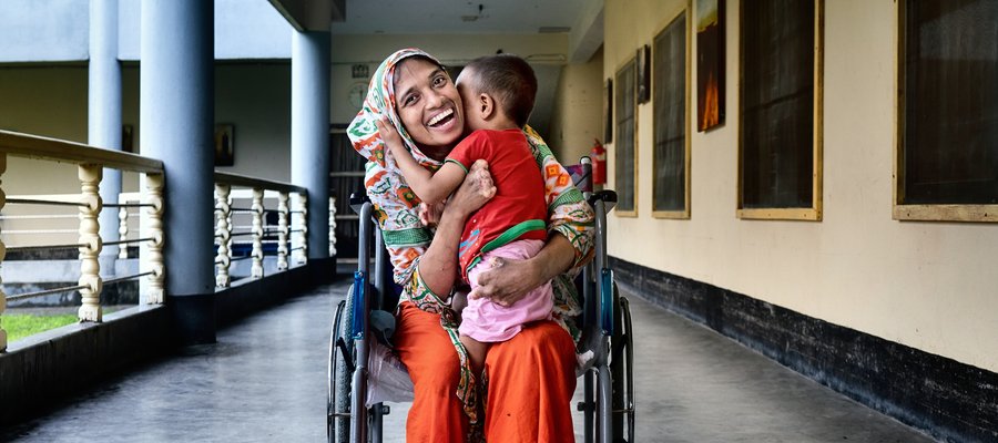 A woman in a wheelchair in Bangladesh hugs her child and smiles