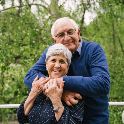 An older couple smile at the camera while embracing