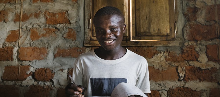A young man with a book smiles at the camera in DR Congo