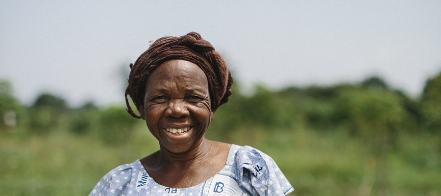 A women in DR Congo holds crops and smiles at the camera