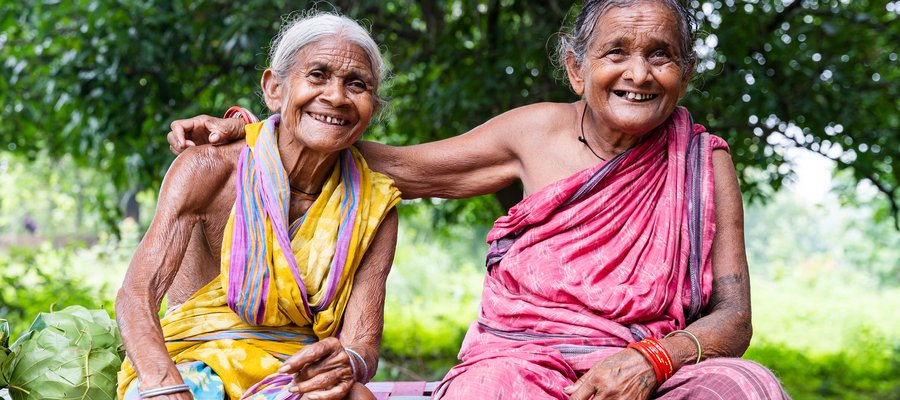 Two older ladies from India sit on a bench, one has her arm around the shoulders of the other