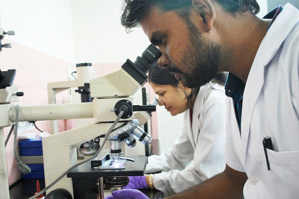 A lab technician in India looks through a microscope