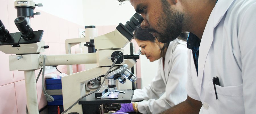 A lab technician in India looks through a microscope