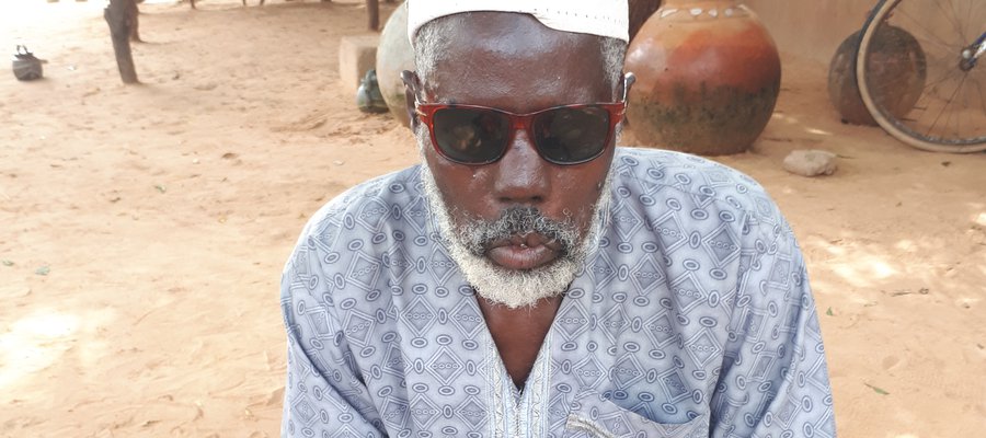 A man affected by leprosy in Niger sits on a mat, wearing sunglasses. He lost his site due to leprosy.