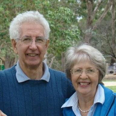 A couple with white hair and glasses smile at the camera together