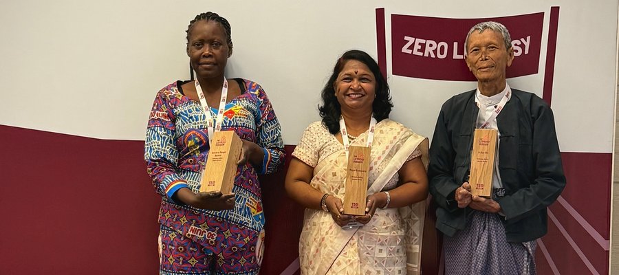 African man and woman, standing and showing their Wellesley Bailey Award trophies.